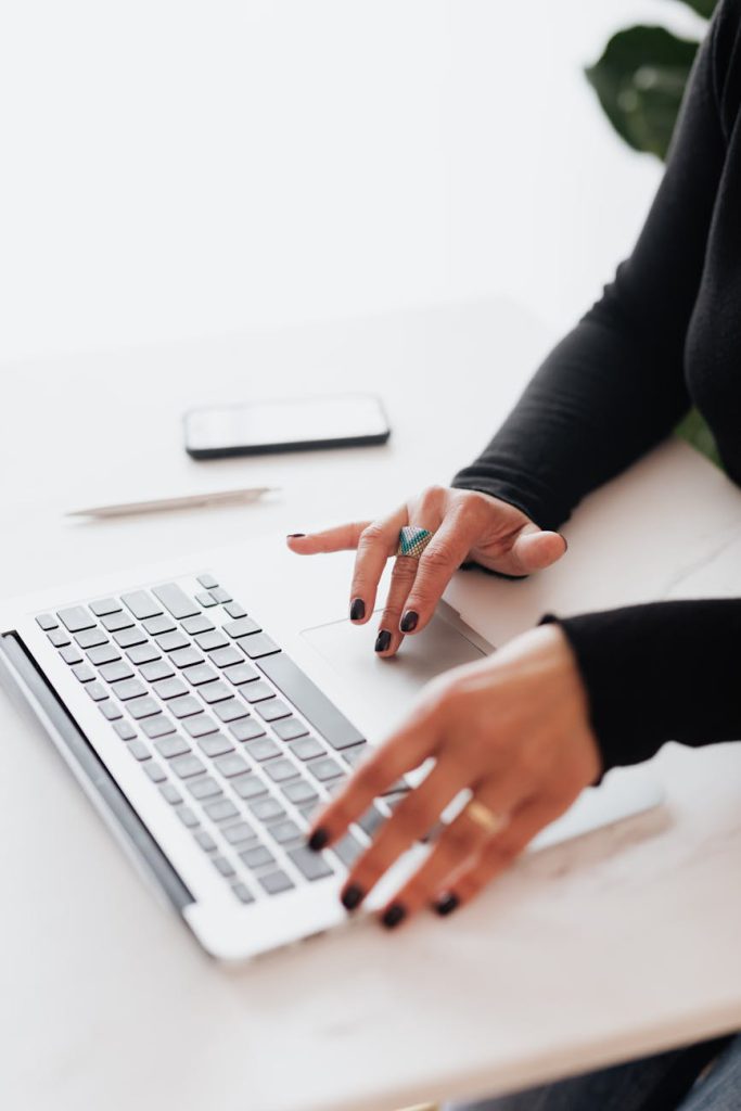 Eine Person tippt auf einer Laptop-Tastatur, während ein Smartphone und ein Stift daneben auf einem weißen Tisch liegen. Das Bild ist das Symbol für professionelle Website-Erstellung und SEO-Strategien für Unternehmen.
