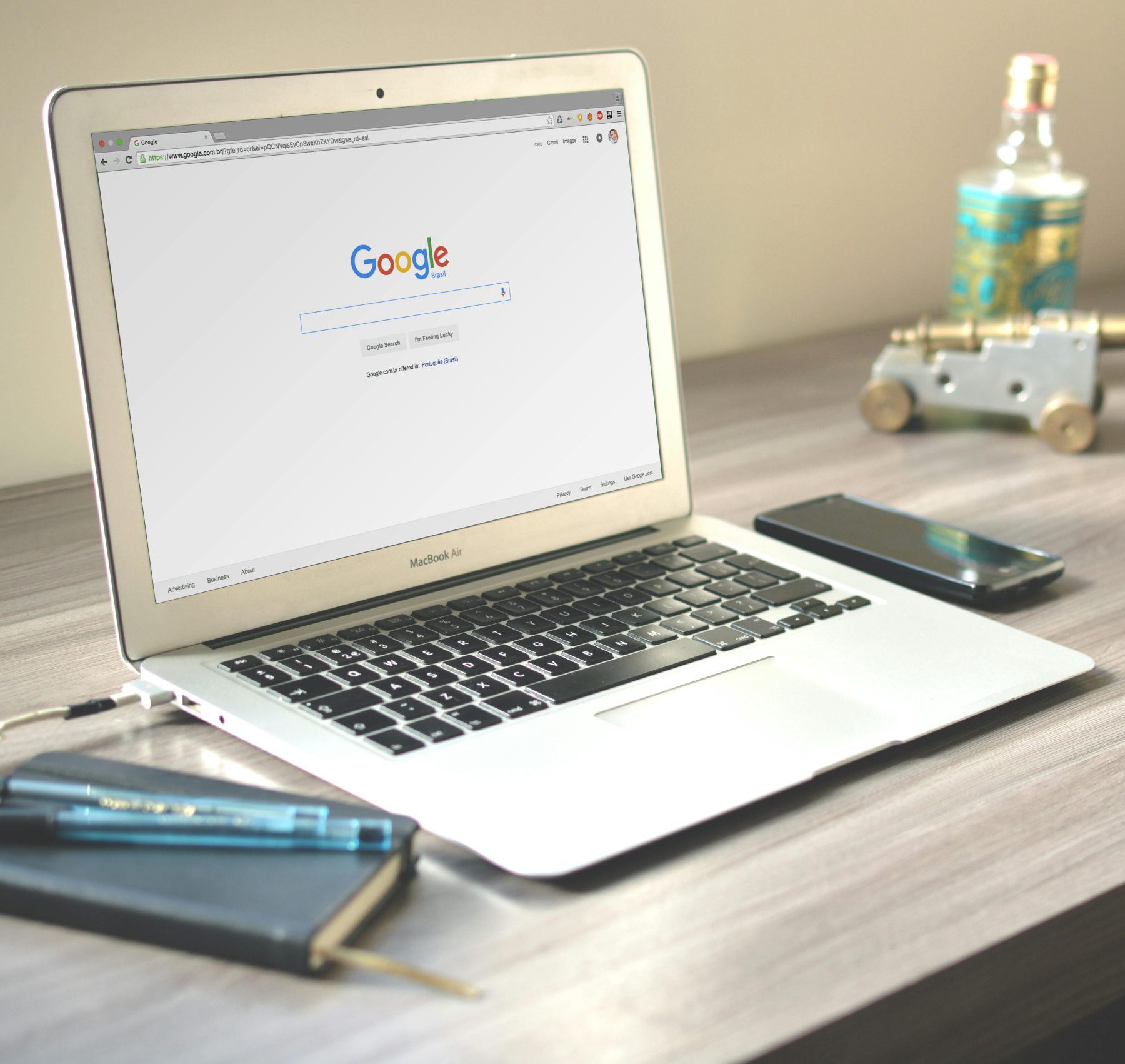 Ein Laptop auf einem Holzschreibtisch zeigt die Google-Startseite, symbolisch für SEO-Strategien und individuelle Websites für Unternehmen. Daneben liegen ein Notizbuch, Stifte und ein Smartphone.